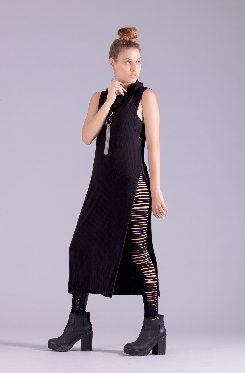 May include: A woman wearing a black maxi dress with a side slit and black leggings with cutouts. She is wearing black heeled boots and has her hair pulled back in a bun.