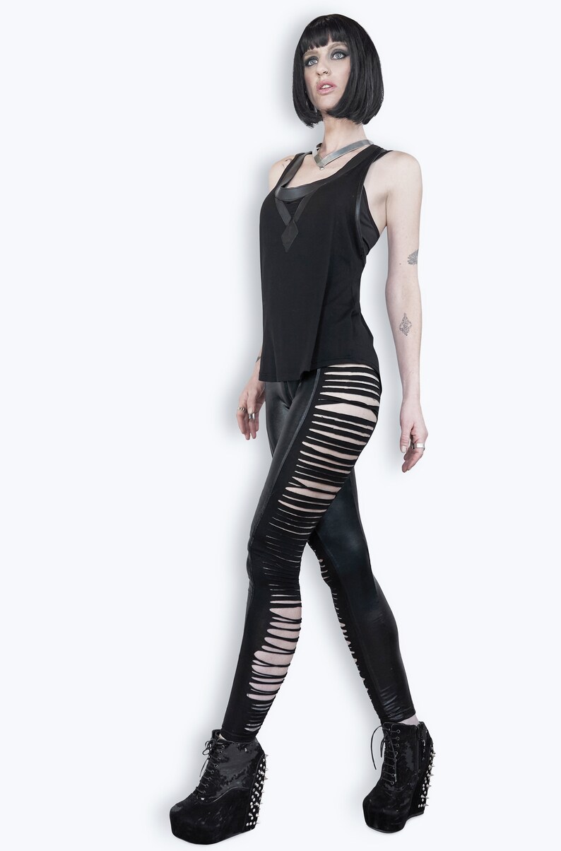 May include: A woman wearing a black tank top with a black leather-look leggings with cutouts on the side. She is wearing black platform boots with silver studs.