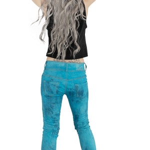 May include: A person wearing blue jeans with a tie-dye pattern, a black tank top, and black combat boots. The person has long, wavy, silver hair.