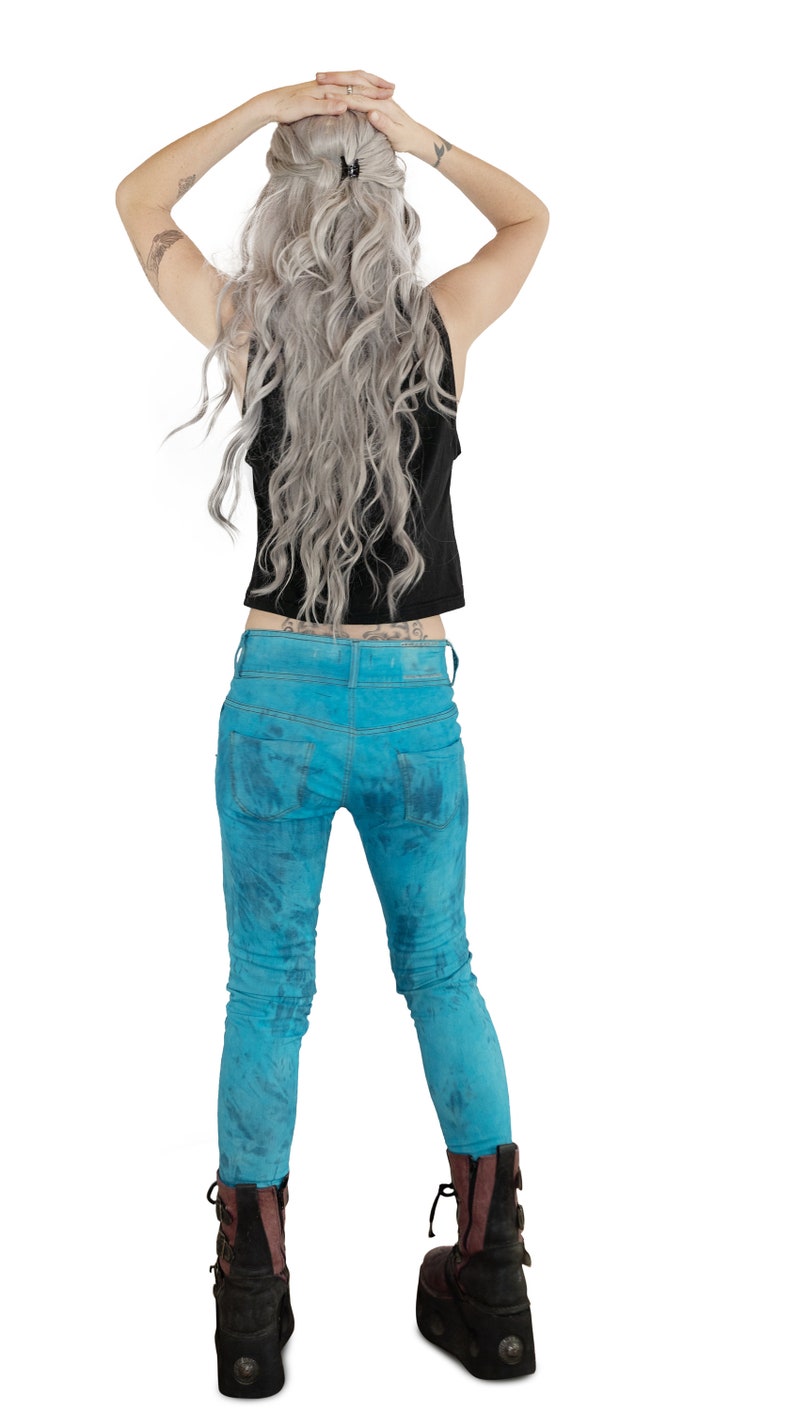 May include: A person wearing blue jeans with a tie-dye pattern, a black tank top, and black combat boots. The person has long, wavy, silver hair.