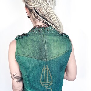 May include: A green denim vest with a gold-colored musical note design on the back. The vest has a studded collar and is sleeveless.