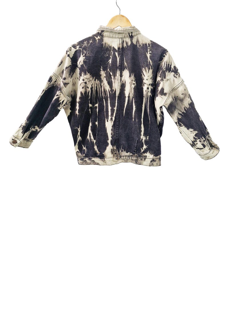 May include: A denim jacket with a unique tie-dye pattern in shades of black and white. The jacket features a classic collar, button-down front, and long sleeves. The tie-dye design creates a striking visual effect, making it a standout piece.