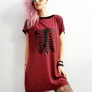 May include: A maroon t-shirt dress with a black ribcage graphic print. The dress has a black trim around the neckline and short sleeves.