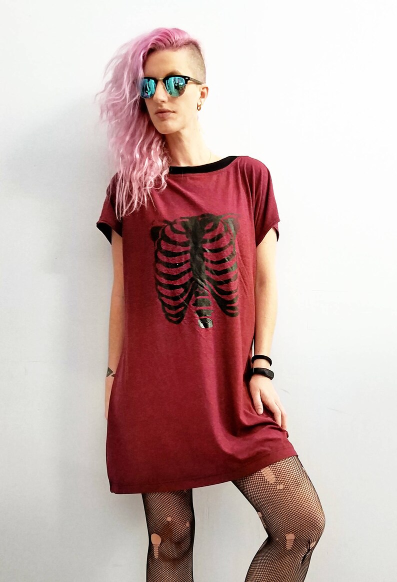 May include: A maroon t-shirt dress with a black ribcage graphic print. The dress has a black trim around the neckline and short sleeves.
