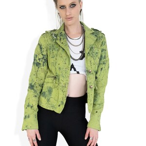 May include: A woman wearing a green splatter-painted jacket with black leggings and multiple silver necklaces.