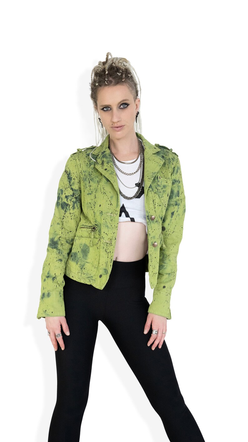May include: A woman wearing a green splatter-painted jacket with black leggings and multiple silver necklaces.