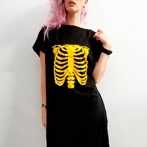 May include: A black t-shirt dress with a yellow skeleton ribcage graphic. The model is wearing black fishnet tights with holes.