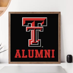 May include: Framed wall art featuring a bold red and white "T" logo on a black background, with the word "ALUMNI" in red below. The artwork has a wooden frame and is displayed on a white surface.