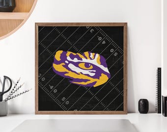 May include: Framed artwork featuring a stylized eye design in purple, yellow, and white, set against a black background with football field markings. The artwork is in a wooden frame.