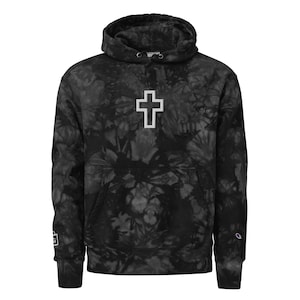 May include: Black tie-dye hoodie with a white cross graphic on the front. The hoodie has a drawstring hood and a kangaroo pocket.