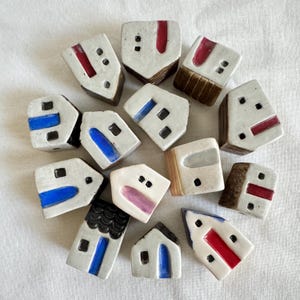 May include: A collection of small, ceramic house figurines. Each house is white with colorful accents like red, blue, and black. The houses have varying roof and door designs, and are arranged in a circular pattern.