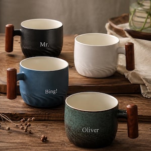 May include: Four ceramic mugs with wooden handles and cream-colored interiors. The black mug is labeled Mr., the blue mug is labeled Bing!, and the green mug is labeled Oliver. Each mug features a textured, wavy pattern around the lower exterior.