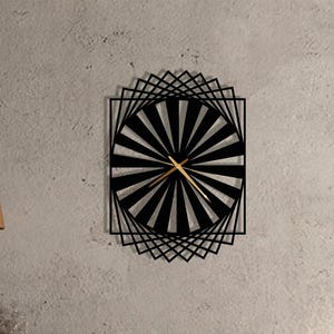 May include: A black and gold geometric wall clock with a sunburst design. The clock is rectangular with a square frame and gold hands. The clock is mounted on a gray wall above a wooden cabinet.