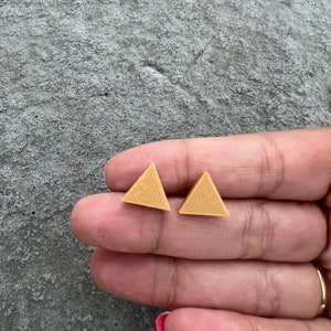 May include: A pair of small, gold triangle earrings. The earrings are made of a textured material and are about 1 cm in size.