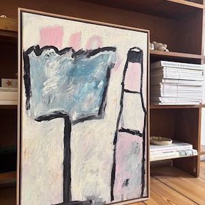 Könnte beinhalten: Abstraktes Gemälde auf Leinwand mit hellem Holzrahmen. Das Kunstwerk zeigt eine blau-weiße, glasähnliche Form und eine rosa-schwarze Flaschenform. Der Hintergrund ist cremefarben mit rosa Akzenten.
