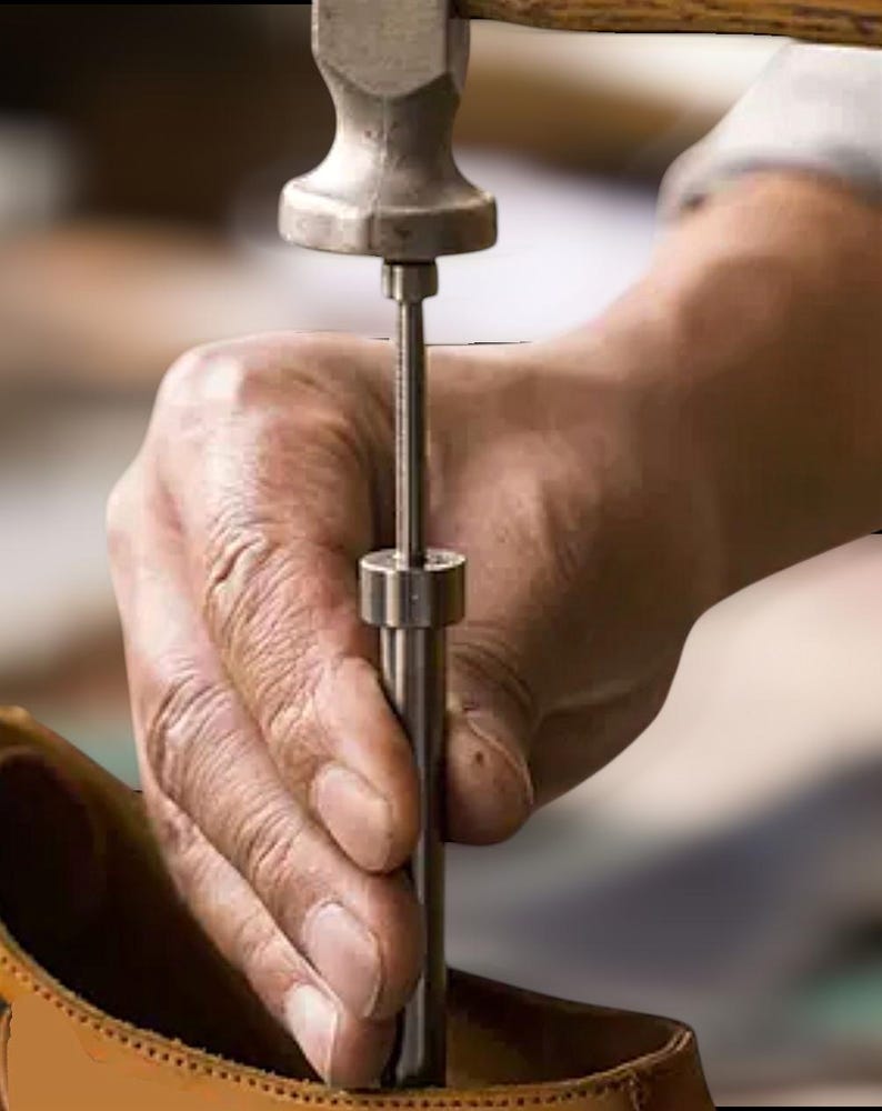 K&ouml;nnte beinhalten: Nahaufnahme einer Hand, die ein Lederbearbeitungswerkzeug h&auml;lt, ein Hammer wird verwendet, um einen Metallstichel in ein St&uuml;ck Leder zu treiben.