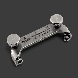 May include: A silver metal ring sizer tool with a graduated scale in centimeters. The tool has two knobs on either end and two rollers. The scale reads from 11 to 17 mm. The tool is labeled "Nattools" and "Made in Italy".