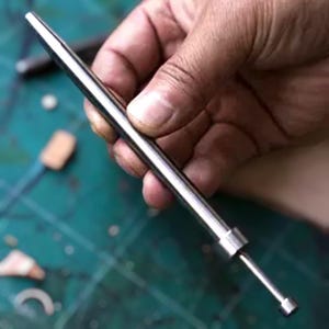 K&ouml;nnte beinhalten: Ein silbernes Werkzeug aus Metall mit einer spitzen Spitze und einem abgerundeten Griff. Das Werkzeug wird in einer Hand gehalten.