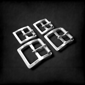 Może przedstawiać: Cztery srebrne metalowe klamry do paska w różnych rozmiarach. Klamry są wszystkie prostokątne z dwoma otworami po każdej stronie. Klamry są ułożone w kształt kwadratu.