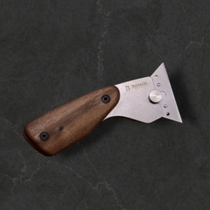 May include: A silver utility knife with a wooden handle. The blade is angled and has a small knob on the side. The handle is made of dark wood and has two small screws. The knife is labeled "Nattools" on the blade.