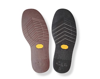 May include: A pair of brown and black shoe soles with a yellow Vibram logo. The soles have a textured pattern and are designed for outdoor use.