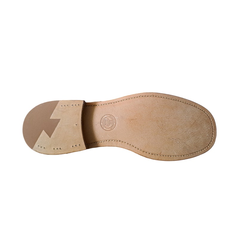 Pu&ograve; includere: Il fondo di una scarpa in pelle marrone con un bordo cucito e un piccolo logo.