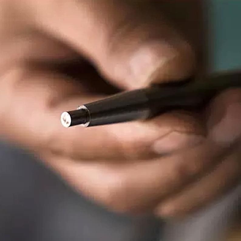 K&ouml;nnte beinhalten: Nahaufnahme eines schwarzen Stifts mit silberner Spitze. Der Stift wird von einer Hand gehalten, aber die Hand ist unscharf.