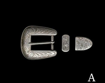 May include: Silver belt buckle with an engraved floral design. The buckle is accompanied by two smaller pieces with matching engravings.