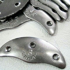 May include: A collection of silver-toned metal shoe heel plates, each featuring a curved, crescent-like shape with three pre-drilled holes for attachment. The surface of each plate is embossed with the number 3 and the word TRIUMPH.