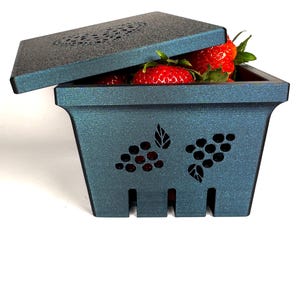 May include: A dark blue, square-shaped, ceramic berry basket with a lid. The basket has a grapevine design and is filled with fresh strawberries.