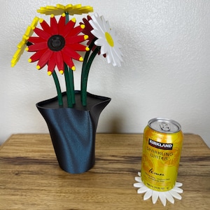 May include: A dark blue vase holds a bouquet of wooden flowers in red, yellow, and white. A yellow can of sparkling water sits on a white daisy-shaped coaster. The can is labeled "Kirkland Sparkling Water Lemon".
