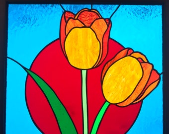May include: Stained glass panel featuring two orange and yellow tulips with green stems and leaves against a red circle and a blue background. The artwork is framed in black.