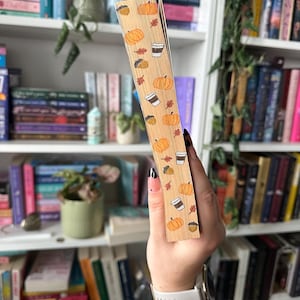 K&ouml;nnte beinhalten: Nahaufnahme eines Buchr&uuml;ckens mit einem Herbst-Design. Der R&uuml;cken ist mit einem hellbraunen Papier mit einem Muster aus K&uuml;rbissen, Kaffeetassen, Eicheln und Bl&auml;ttern bedeckt.