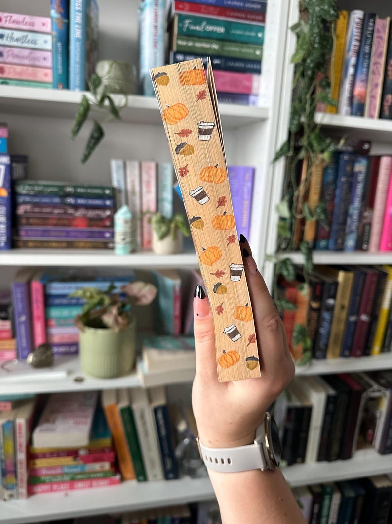K&ouml;nnte beinhalten: Nahaufnahme eines Buchr&uuml;ckens mit einem Herbst-Design. Der R&uuml;cken ist mit einem hellbraunen Papier mit einem Muster aus K&uuml;rbissen, Kaffeetassen, Eicheln und Bl&auml;ttern bedeckt.