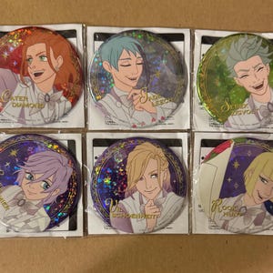 May include: Six round, holographic buttons featuring characters from the anime "Twisted Wonderland". Each button has a different character and their name printed on the button. The characters are Cater Diamond, Jade Leech, Sebek Zigvolt,  Crewel Felmier, Vil Schoenheit, and Rook Hunt.