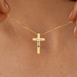 May include: A gold cross pendant necklace with a fine chain. The cross has the inscription "I love you" and is decorated with three colourful gemstones. The necklace is shown against a plain backdrop.