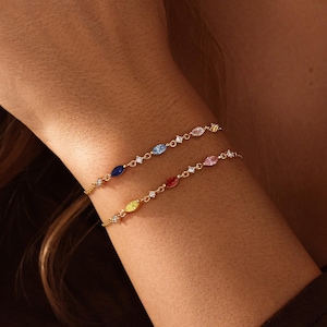 May include: Two gold-tone chain bracelets featuring marquise-cut multicolored gemstones and small clear round stones. The bracelets display a variety of colors including blue, light blue, pink, yellow, and red, arranged along the delicate metal links.