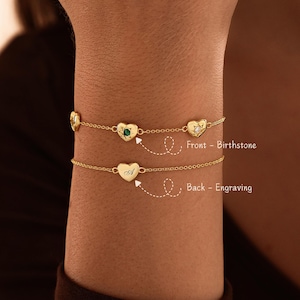 May include: Two gold chain bracelets featuring heart-shaped charms. The top bracelet displays heart charms with inset birthstones. The bottom bracelet features a heart charm with an engraved letter A. Text labels indicate Front - Birthstone and Back - Engraving.