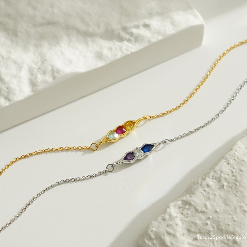 May include: Two delicate bracelets with a pea pod design. One bracelet is gold with blue, green, red, and yellow gemstones. The other bracelet is silver with purple, white, and blue gemstones.