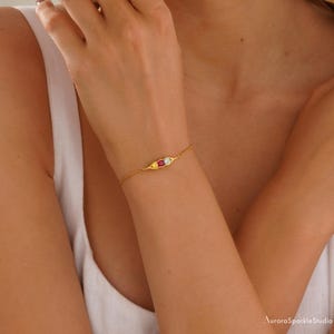 May include: A gold chain bracelet with three small pea pod charms. The charms are decorated with red, yellow, and blue gemstones.