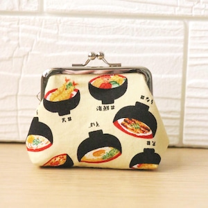 Könnte beinhalten: Beige Münzbörse mit Metallverschluss und einem sich wiederholenden Muster aus schwarzen Ramen-Schalen mit verschiedenen Belägen. Japanische Schriftzeichen sind in der Nähe der Schalen aufgedruckt. Die Börse ist aus Stoff.
