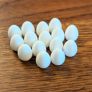 Op de afbeelding: Een verzameling witte, eivormige objecten gerangschikt op een houten oppervlak. De eieren hebben een gladde textuur en zijn gegroepeerd, wat een visueel aantrekkelijke opstelling creëert. Het houten oppervlak biedt een warme, natuurlijke achtergrond.