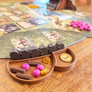 Könnte beinhalten: Ein braunes Holzspieltablett mit der Nummer "3" an der Seite. Das Tablett enthält kleine braune Holzstücke, rosa und gelbe Plastikstücke und braune Holzstäbchen.