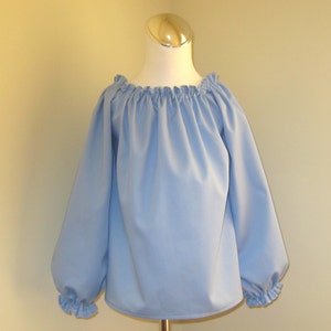 May include: A light blue, long-sleeved blouse with a gathered neckline and ruffled cuffs.