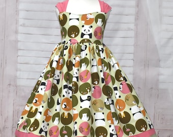 Può includere: Un vestito verde e rosa con un motivo a cerchi che presenta orsi panda, orsi polari e altri animali. Il vestito ha un corpetto rosa e una gonna verde con un bordo rosa e verde.