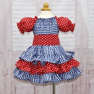 Op de afbeelding: Een blauw en rood ginghamjurk met witte stippen. De jurk heeft een geruite rok en korte pofmouwen.