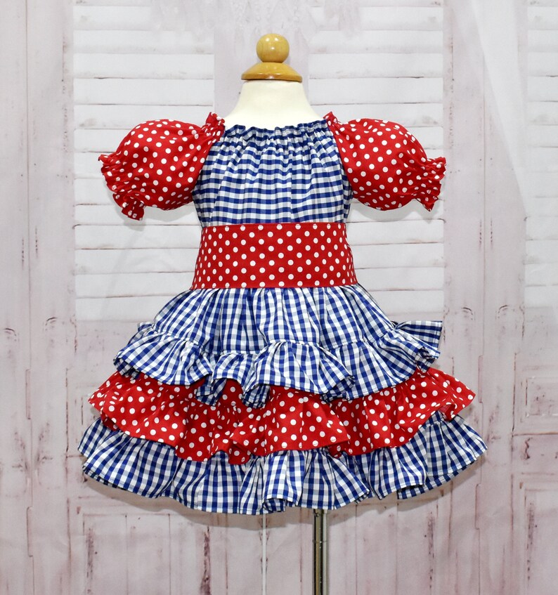 Op de afbeelding: Een blauw en rood ginghamjurk met witte stippen. De jurk heeft een geruite rok en korte pofmouwen.