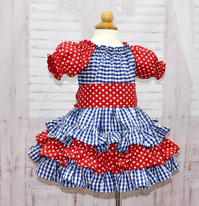Op de afbeelding: Een blauw en rood ruitjesjurk met witte stippen. De jurk heeft een geruite rok en korte mouwen.