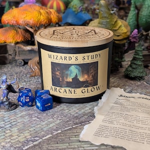 May include: A black candle with a wooden lid, labeled "WIZARD'S STUDY" and "ARCANE GLOW." The label features an illustration of a wizard's study. Three blue dice and a miniature figure are in front of the candle.