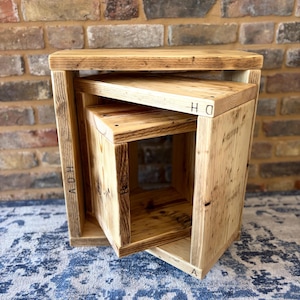 May include: A set of three wooden nesting tables. The tables are made from light-coloured wood and have a rustic, handmade appearance. Each table is a different size, with the smallest fitting inside the largest. The tables are arranged on a blue patterned rug.